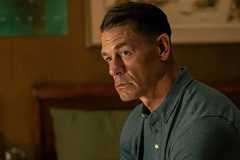 John Cena as Chris looking thoughtfully while sitting on his bed in Peacemaker season 2